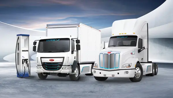 Image of two Peterbilt electric trucks parked in front of an EV charger